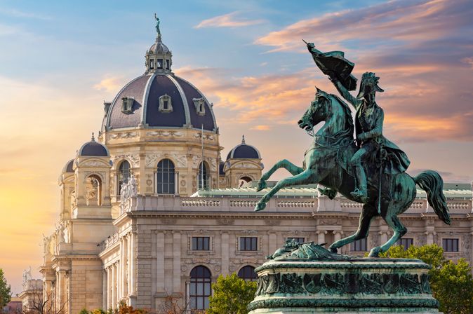 Nationalmuseum in Wien. Davor eine Reiterstatue mit Flagge. Blau-rosa Himmel.