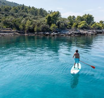 Eine Person steht auf einem Stand-Up-Paddleboard auf klarem, blauem Wasser.
