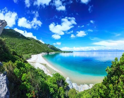 Eine Küstenlandschaft mit einem Strand, Bergen und türkisfarbenem Wasser.
