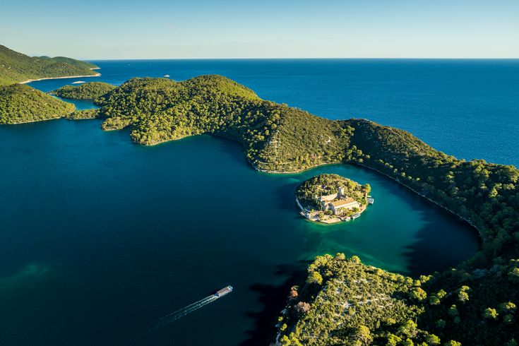 Eine Luftaufnahme einer bewaldeten Küstenlinie mit vielen Buchten und türkisfarbenem Wasser.