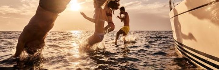 Eine Familie springt ins Wasser vom Boot aus.